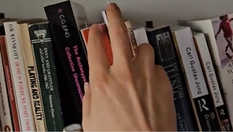 A hand seductively browsing a shelf of books by the psychoanalyst Carl Jung.
